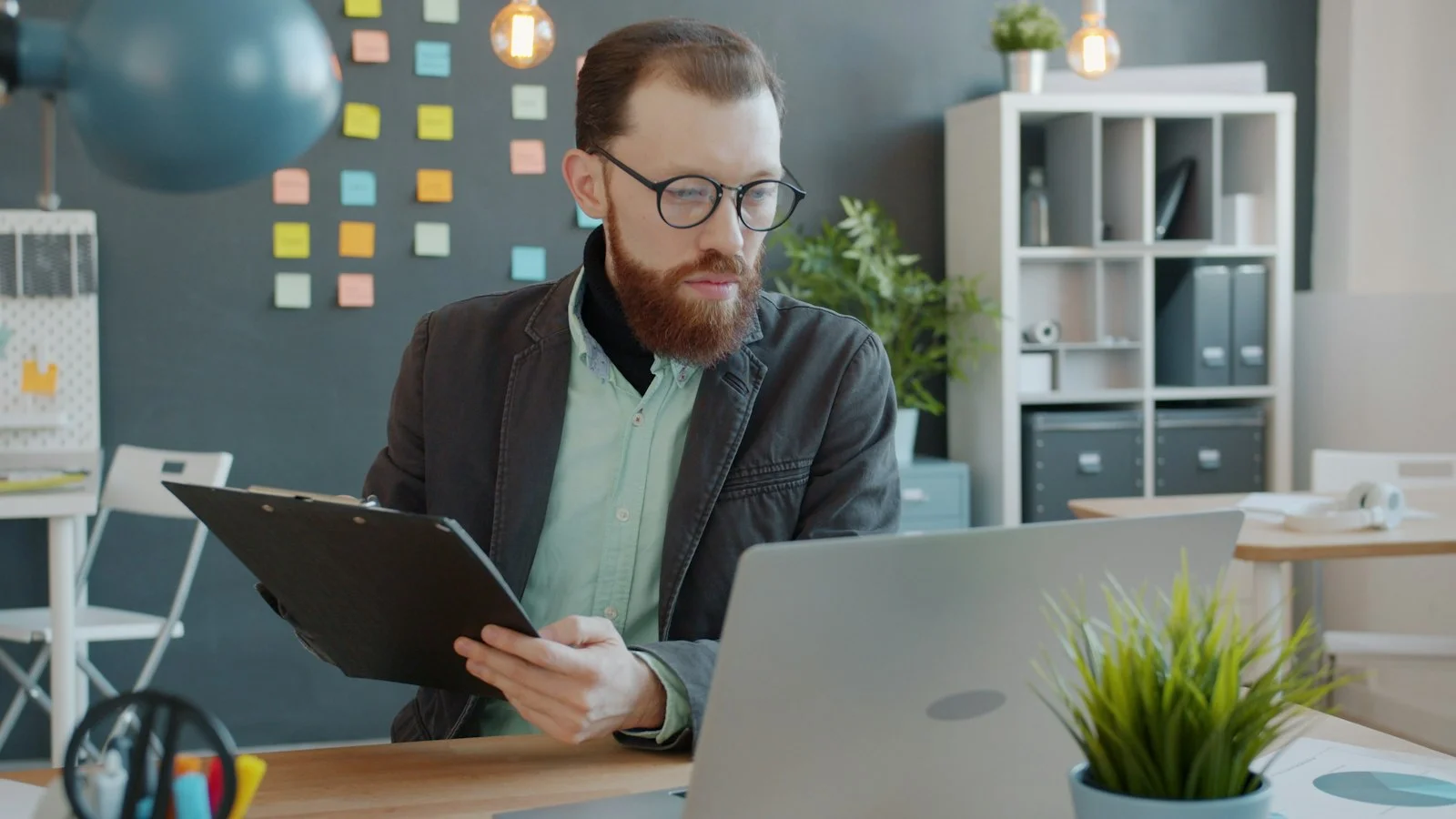 Man with beard working on laptop and clipboard Man with beard working on laptop and clipboard