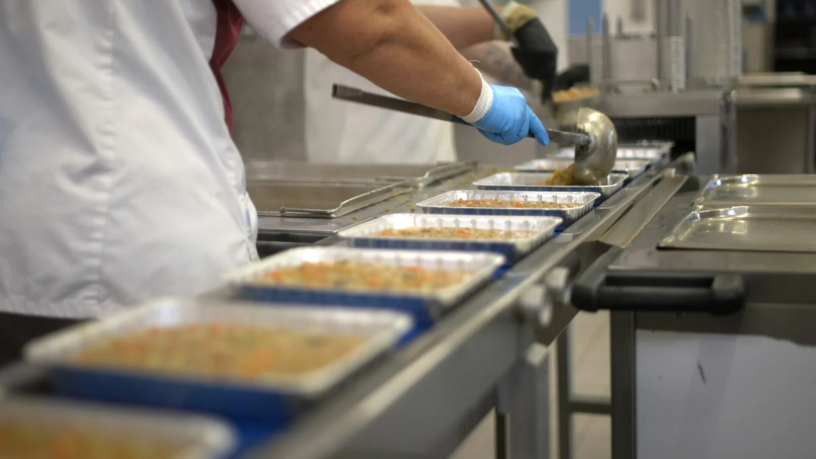 Worker filling food trays on a conveyor belt Worker filling food trays on a conveyor belt